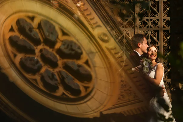 Adorável noivo e noiva beijando e segurando fora, com uma reflexão da igreja — Fotografia de Stock