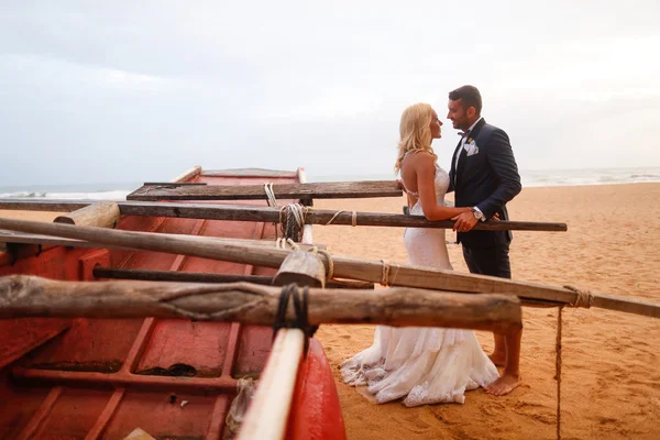 Sposa e sposo baciare sulla spiaggia vicino a una barca di legno — Foto Stock