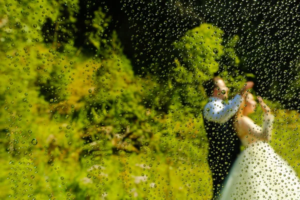 Braut und Bräutigam posieren durch eine nasse Linse — Stockfoto