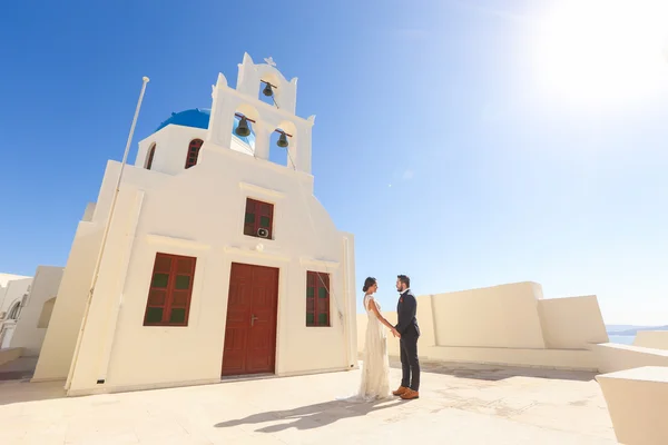 Νύφη και ο γαμπρός που παρουσιάζουν κοντά σε μια άσπρη εκκλησία — Φωτογραφία Αρχείου