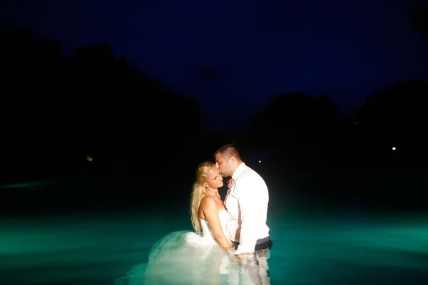 Bruden och brudgummen poserar i vatten på natten — Stockfoto