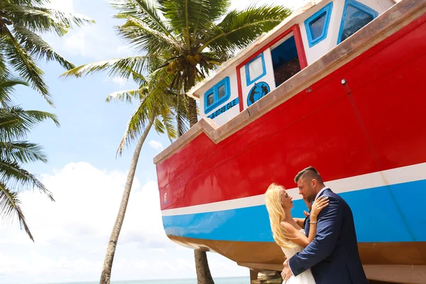 Novio y novia besándose en la playa cerca de un barco de madera —  Fotos de Stock