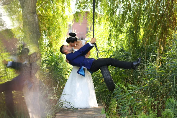 Beautiful bridal couple having fun on a swing — Stock Photo, Image