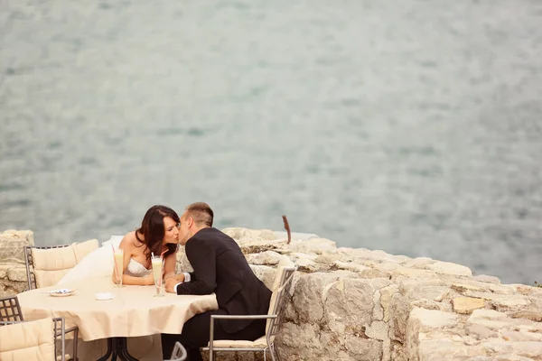 海の横にあるテーブルでキスする新郎新婦 — ストック写真