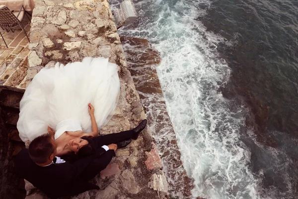 Happy bridal couple laying on stones next to the sea — Stock Photo, Image