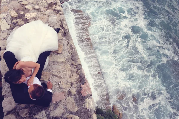 Happy bridal couple laying on stones next to the sea — Stock Photo, Image