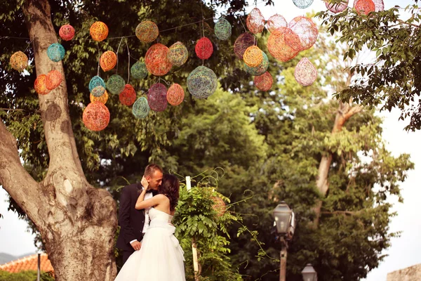 Bride and groom kissing under colorful lamps — Stock Photo, Image