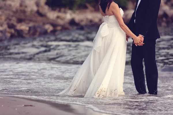Bruid en bruidegom hand in hand op het strand — Stockfoto