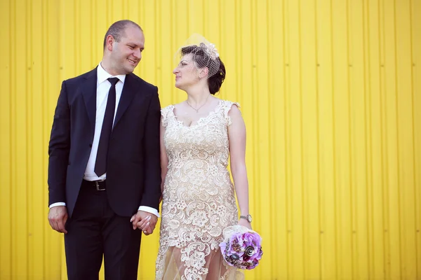 Bruid en bruidegom hand in hand in de buurt van geel muur — Stockfoto