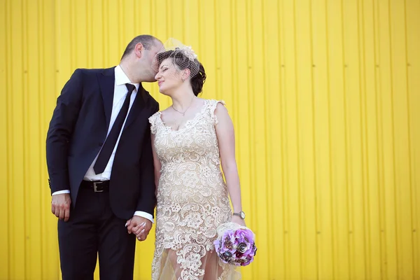 Bride and groom holding hands near yellow wall — Stock Photo, Image