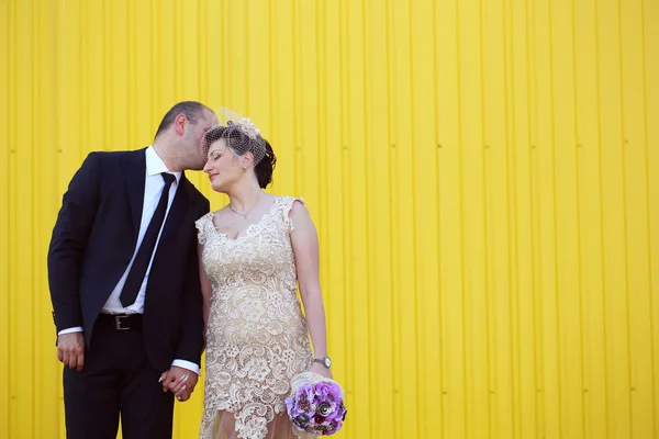 Mariée et marié tenant la main près du mur jaune — Photo