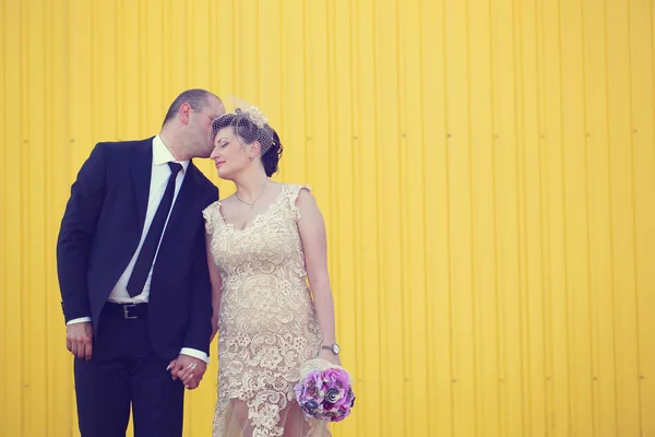 Bruden och brudgummen håller hand nära gula väggen — Stockfoto