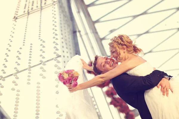 Groom picking up his bride on bridge — Stock Photo, Image