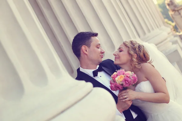 Bride and groom holding each other near columns — Stock Photo, Image