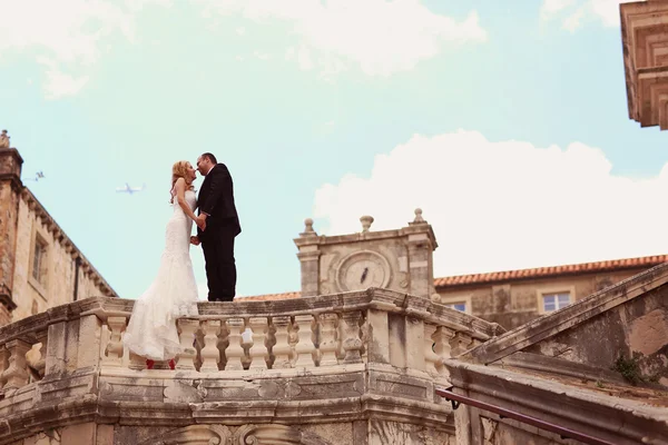 Bride and groom sitting on stone fence in a castle — Stock Photo, Image