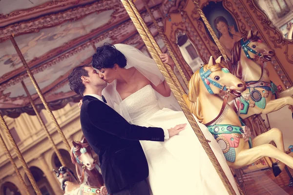 Gelukkige bruid en bruidegom kussen op carrousel — Stockfoto
