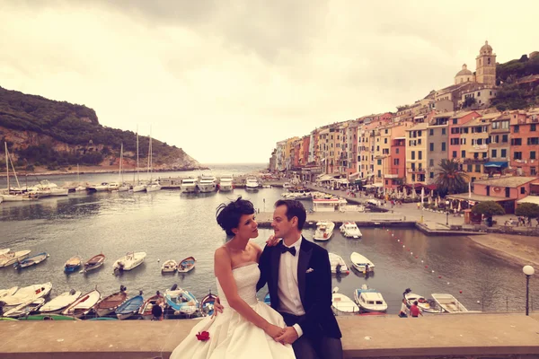 Bride and groom on bridge with boats in background — Stock Photo, Image