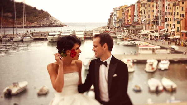 Bride and groom on bridge with boats in background — Stock Photo, Image