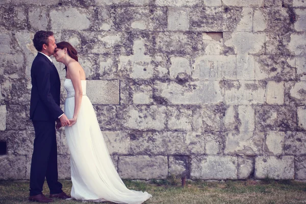 Noiva e noivo beijando perto da parede de tijolo — Fotografia de Stock