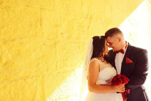 Bride and groom on a yellow wall in the sunlight — Stock Photo, Image