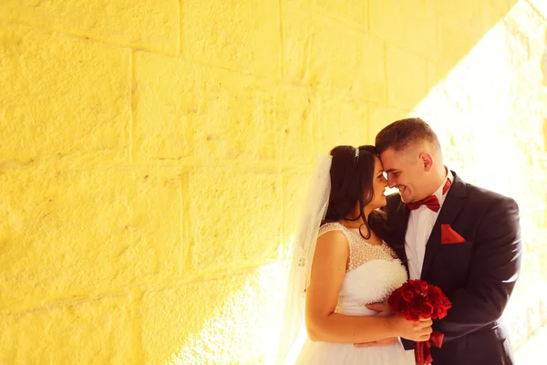 Mariée et marié sur un mur jaune à la lumière du soleil — Photo