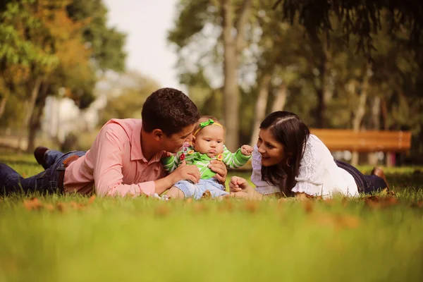 Föräldrar med baby flicka sitter på gräset i parken — Stockfoto