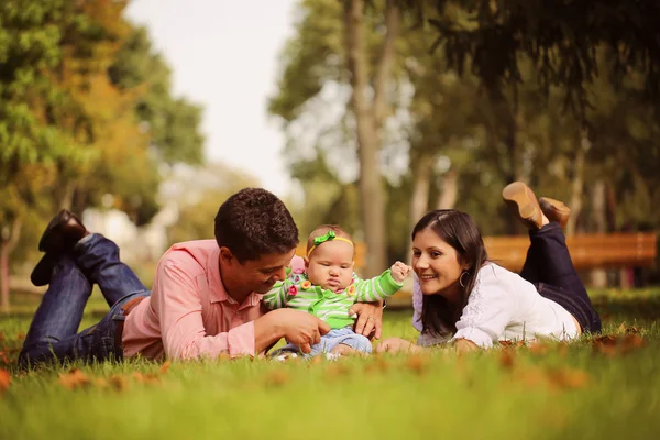 Los padres con la niña sentada en la hierba en el parque — Foto de Stock