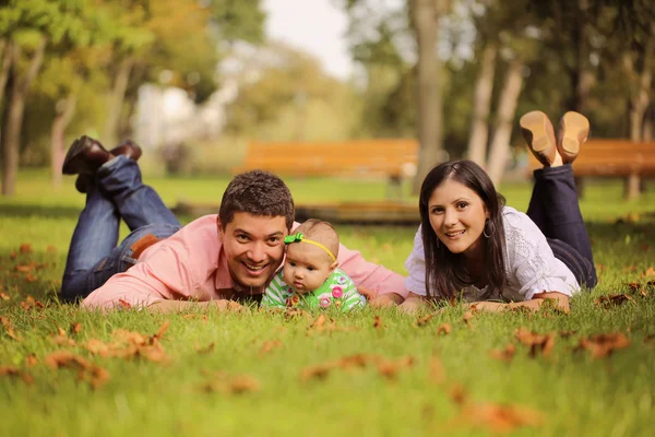 Los padres con la niña sentada en la hierba en el parque — Foto de Stock