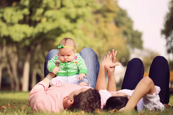 Les parents s'allongent tenant sa petite fille vers le haut — Photo