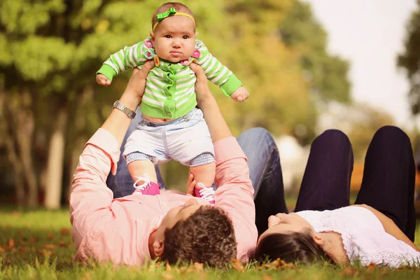 Parents lie down holding her baby girl up — Stock Photo, Image