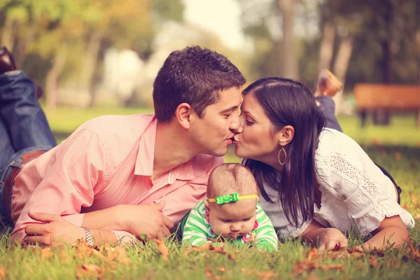 Föräldrar med baby flicka sitter på gräset i parken — Stockfoto