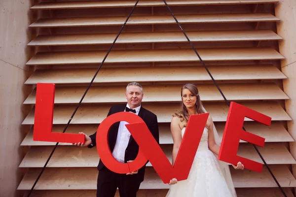 Novia y novio sosteniendo grandes letras rojas de AMOR — Foto de Stock