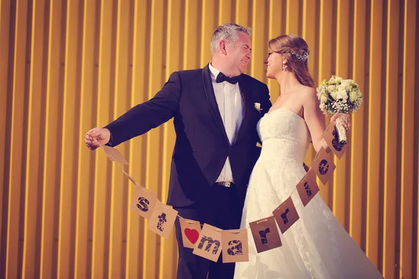 Bride and groom having fun against a yellow wall — Stock Photo, Image