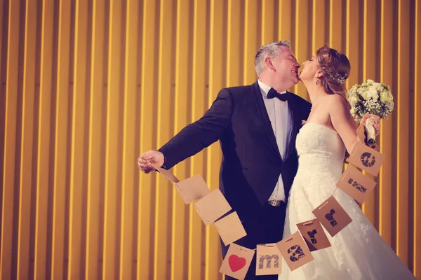 Bruden och brudgummen ha roligt mot en gul vägg — Stockfoto