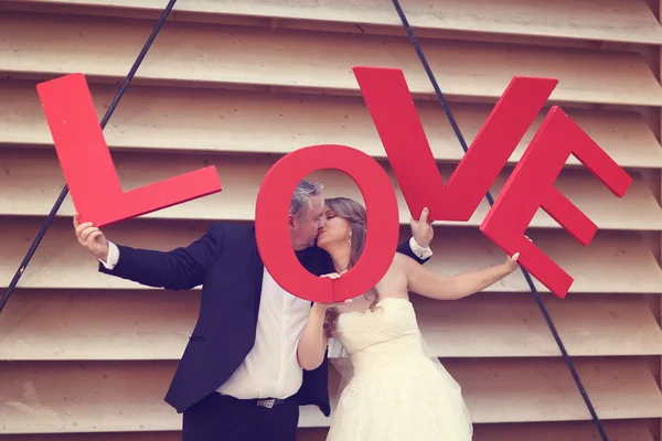 Bride and groom holding big red LOVE letters — Stock Photo, Image