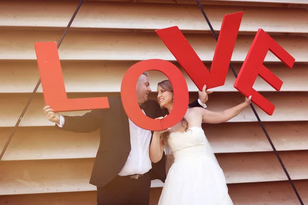 Bride and groom holding big red LOVE letters — Stock Photo, Image