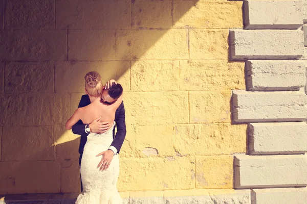 Bruid en bruidegom faceing een geel muur — Stockfoto