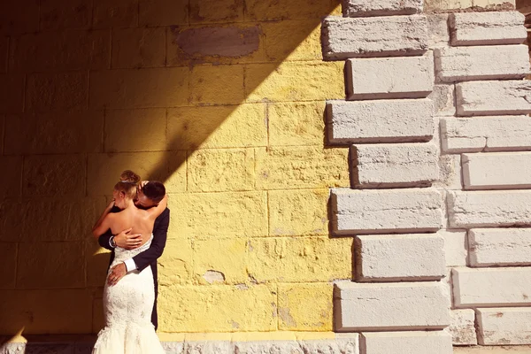 Noiva e noivo de frente para uma parede amarela — Fotografia de Stock