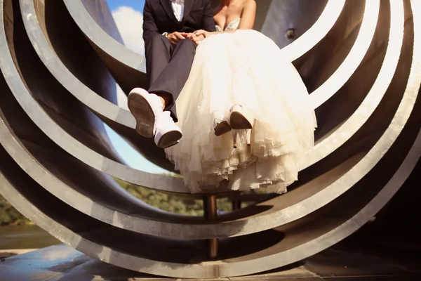 Νύφη και ο γαμπρός κάθεται σε αρχιτεκτονικά μεταλλικό κομμάτι — Φωτογραφία Αρχείου