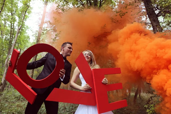 Bruid en bruidegom houden grote Love letters in het bos, omringd door rode rook — Stockfoto