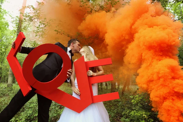 Mariée et marié tenant de grandes lettres d'AMOUR dans la forêt, entourée de fumée rouge — Photo