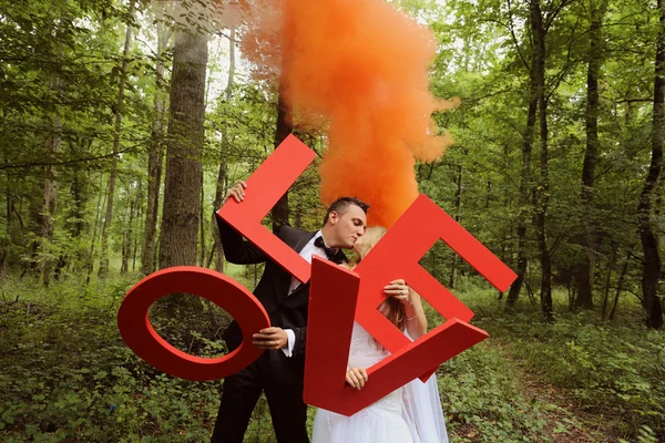 Bruid en bruidegom houden grote Love letters in het bos, omringd door rode rook — Stockfoto