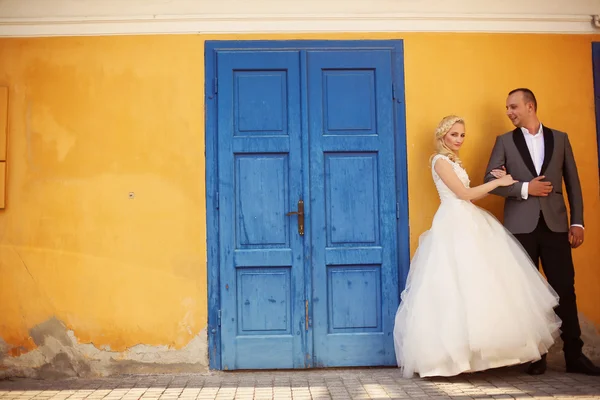 Bride and groom against yellow wall and blue door — Stock Photo, Image