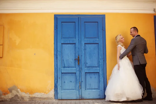 Bride and groom against yellow wall and blue door — Stock Photo, Image