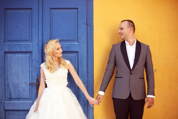 Noiva e noivo contra parede amarela e porta azul — Fotografia de Stock