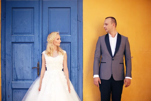 Bride and groom against yellow wall and blue door — Stock Photo, Image