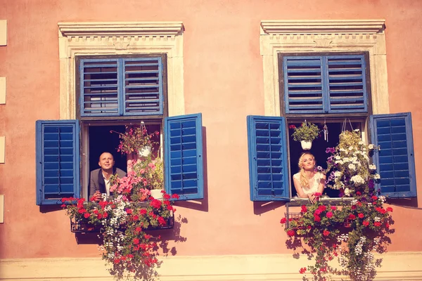 Nevěsta a ženich baví z okna ze starého domu — Stock fotografie