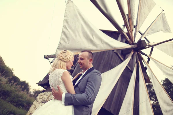 Novia y novio posando en un hermoso paisaje, cerca de un molino de viento —  Fotos de Stock