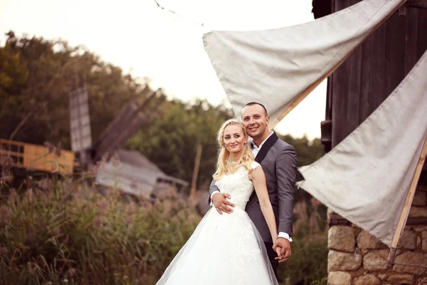 Braut und Bräutigam posieren in einer wunderschönen Landschaft, in der Nähe einer Windmühle — Stockfoto