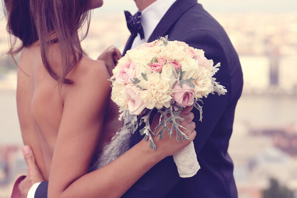 Detail of a bride and groom embracing. Bride holding beautiful wedding bouquet